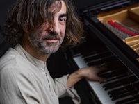a man with long hair sitting at a piano